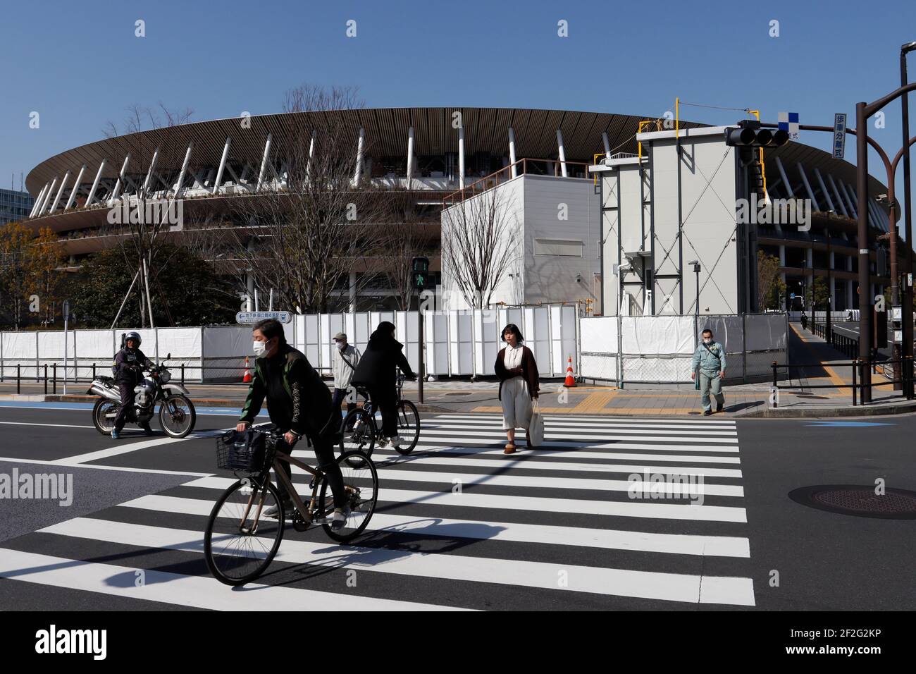 Tokio, Japan. März 2021, 12th. Radfahrer fahren an einem Schild der Olympischen Spiele 2020 in Tokio vorbei, auf dem Bürgersteig vor dem Nationalstadion, dem Hauptstadion der Olympischen Spiele und Paralympics 2020 in Tokio, inmitten einer Pandemie des Jahres 19. Kredit: SOPA Images Limited/Alamy Live Nachrichten Stockfoto