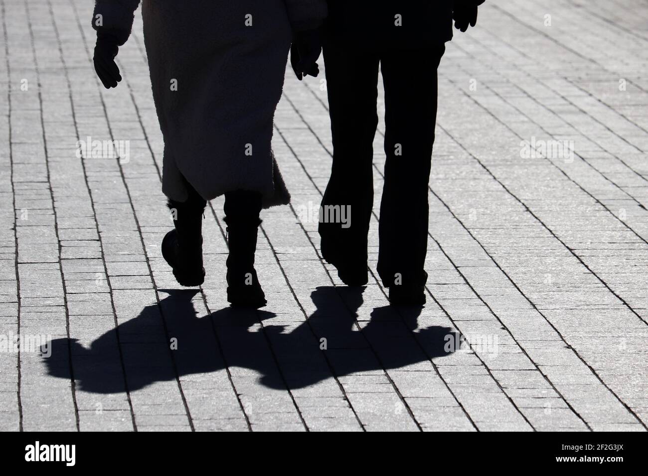 Ein Paar, das die Straße entlang geht, Silhouetten und Schatten von zwei Personen auf dem Fußgängerweg. Männliche und weibliche Beine, Beziehungskonzept Stockfoto