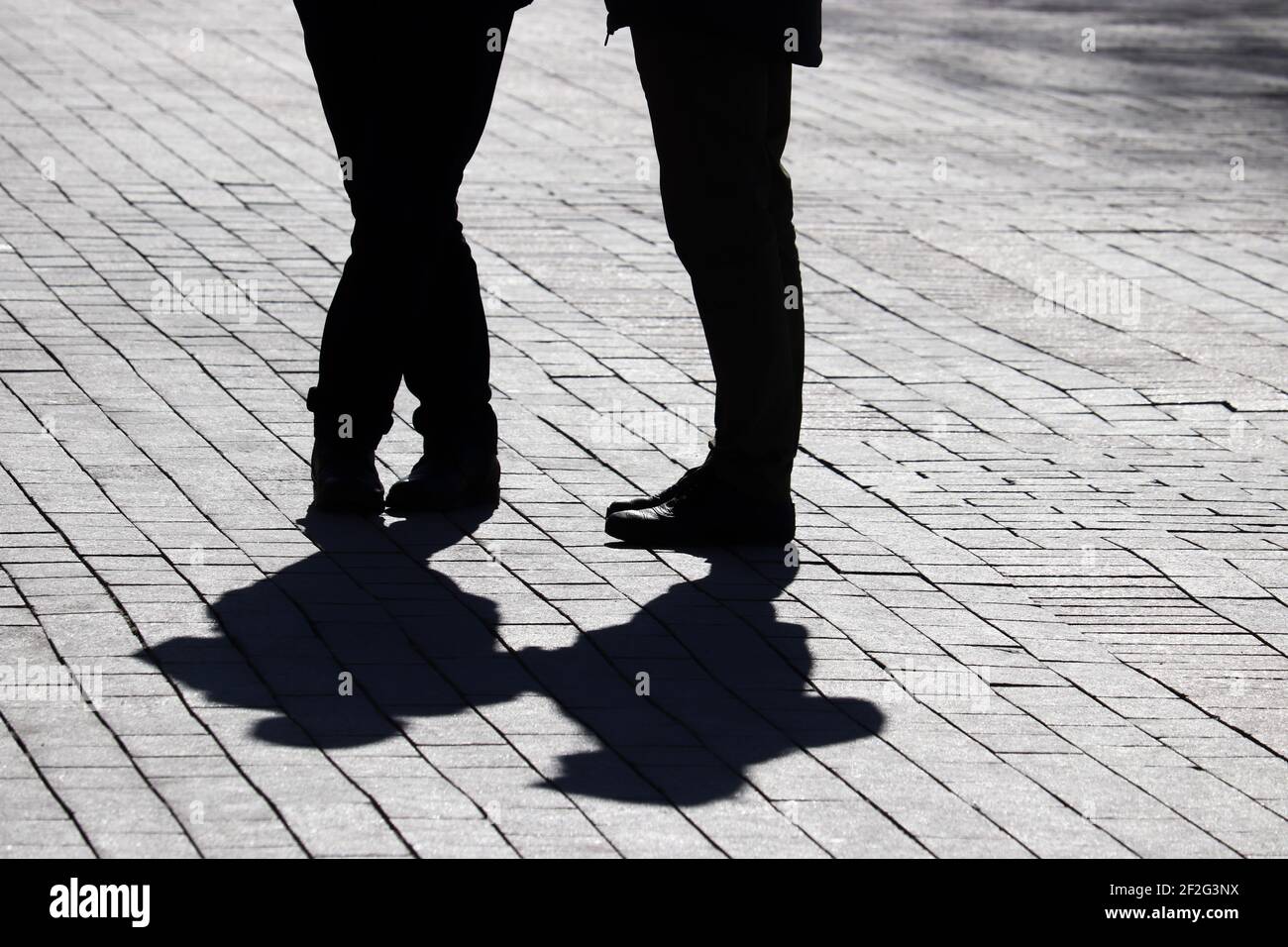 Silhouetten und Schatten eines Paares auf der Straße, zwei Menschen, die auf dem Fußgängerweg stehen. Konzept der Beziehungen, Stadtleben, dramatische Geschichten Stockfoto