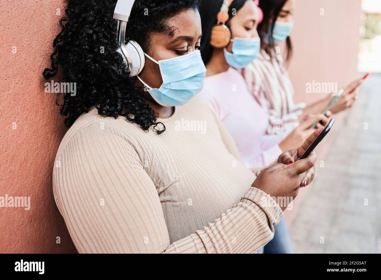 Junge multirassische Freunde tragen Schutzmasken während der Verwendung von Handy Im Freien - Fokus auf der rechten Hand Stockfoto