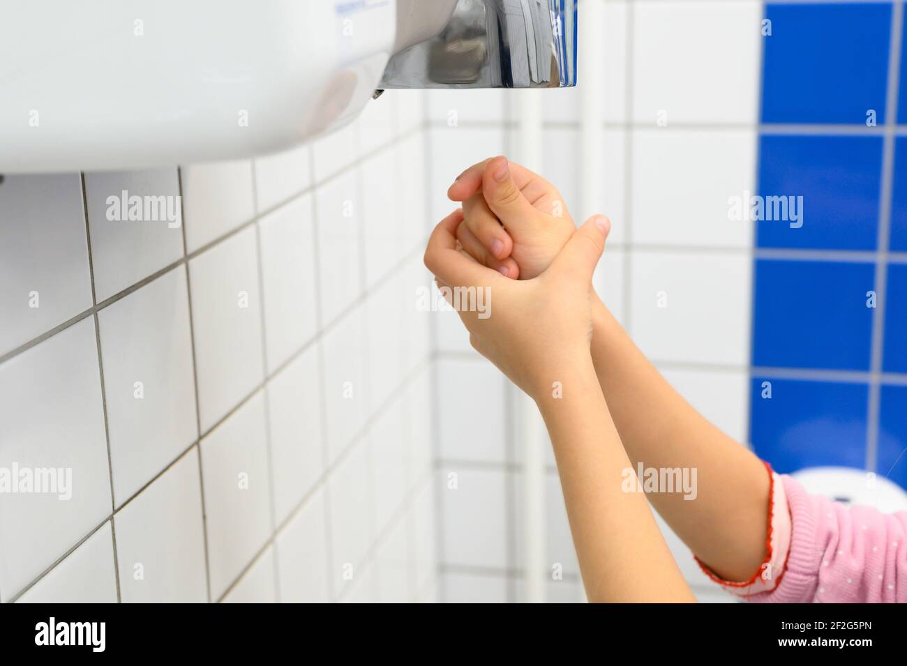 Kinderhände mit Lufttrockner in öffentlichen Toiletten oder Waschräumen Stockfoto