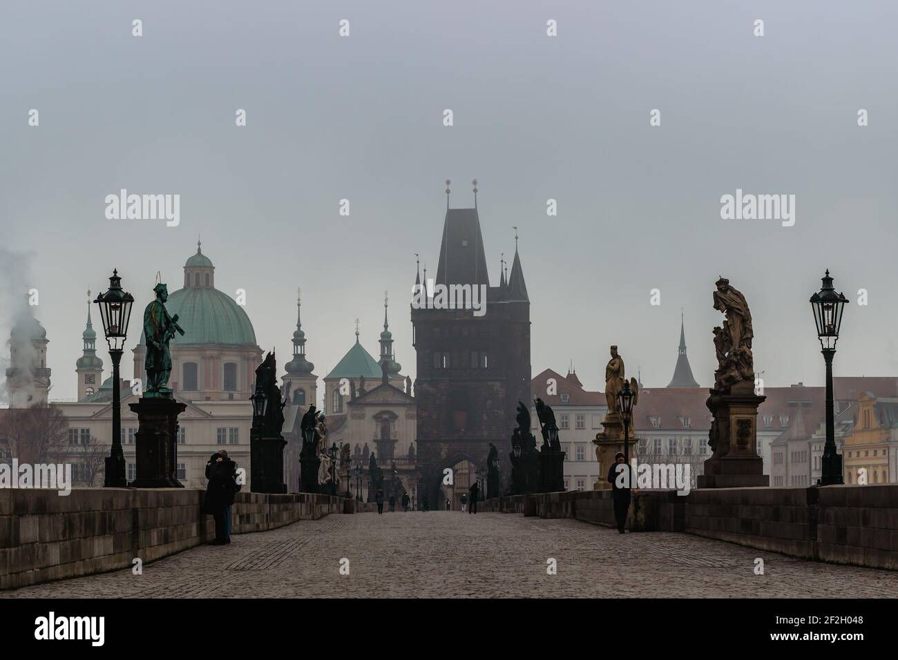 Prag, Tschechische Republik - 24. Februar 2021.Blick auf die Karlsbrücke, Altstädter Brückenturm in kalten nebligen Morgen. Menschen, die durch die Stadt gehen. Stockfoto