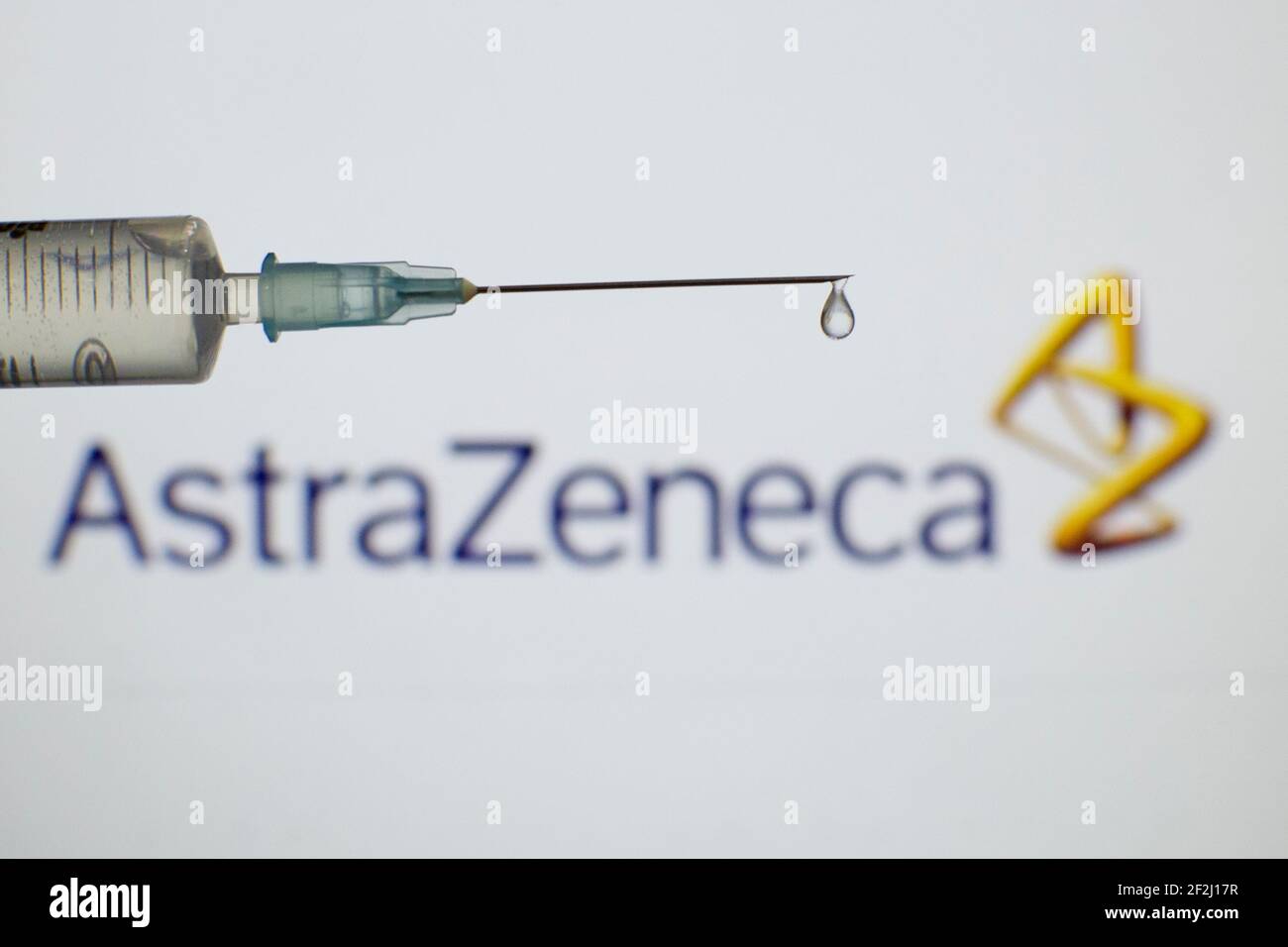 Foto einer medizinischen Spritze mit einem Tropfen, der aus der Nadel kommt, mit dem Firmenlogo des Impfstoffunternehmens AstraZeneca Coronavirus auf einer Beleuchtung Stockfoto