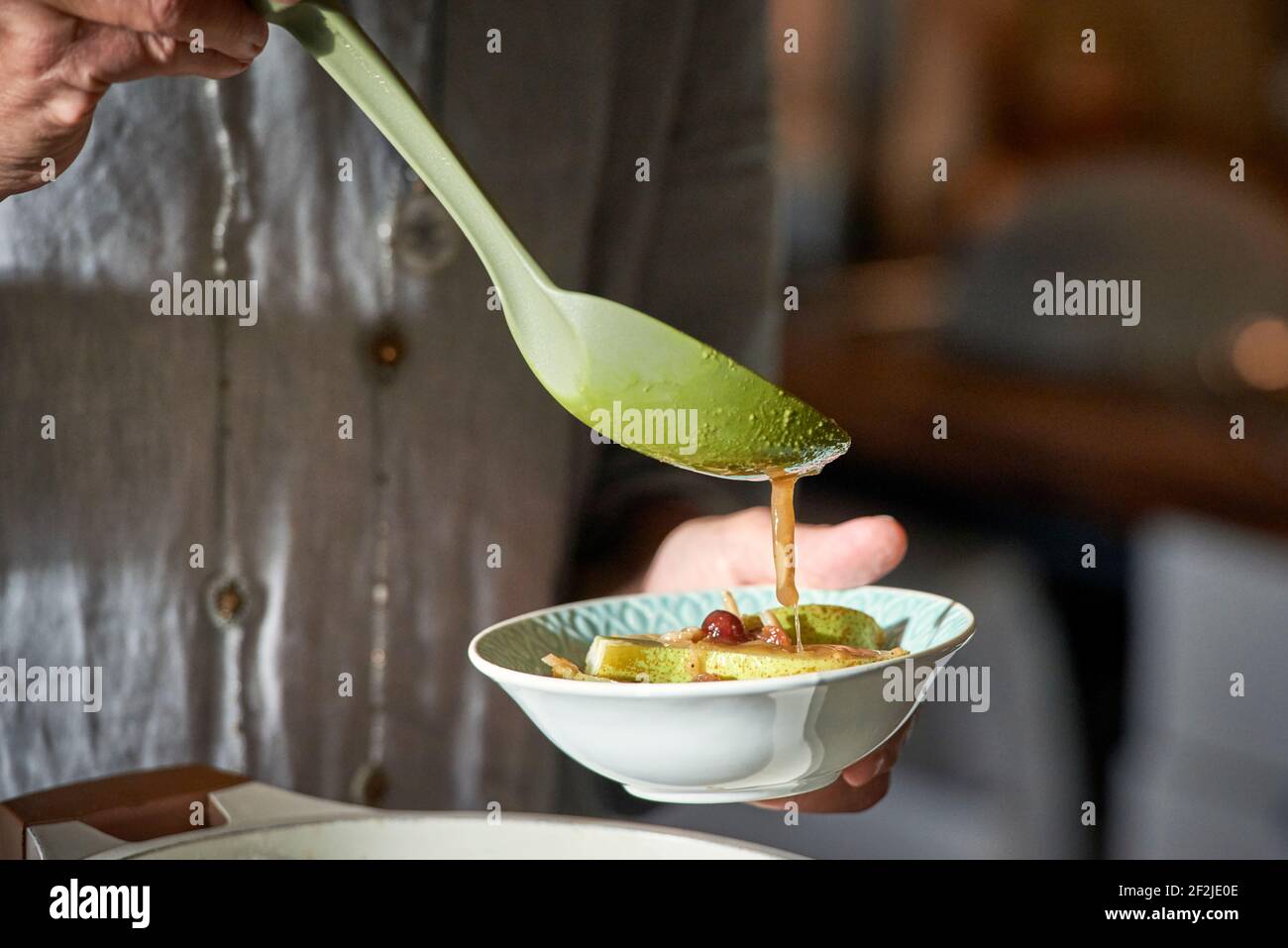Die Hand der Frau gießt Birnenkeile in eine Schüssel mit Gewürzen Sauce mit einem großen Löffel Stockfoto