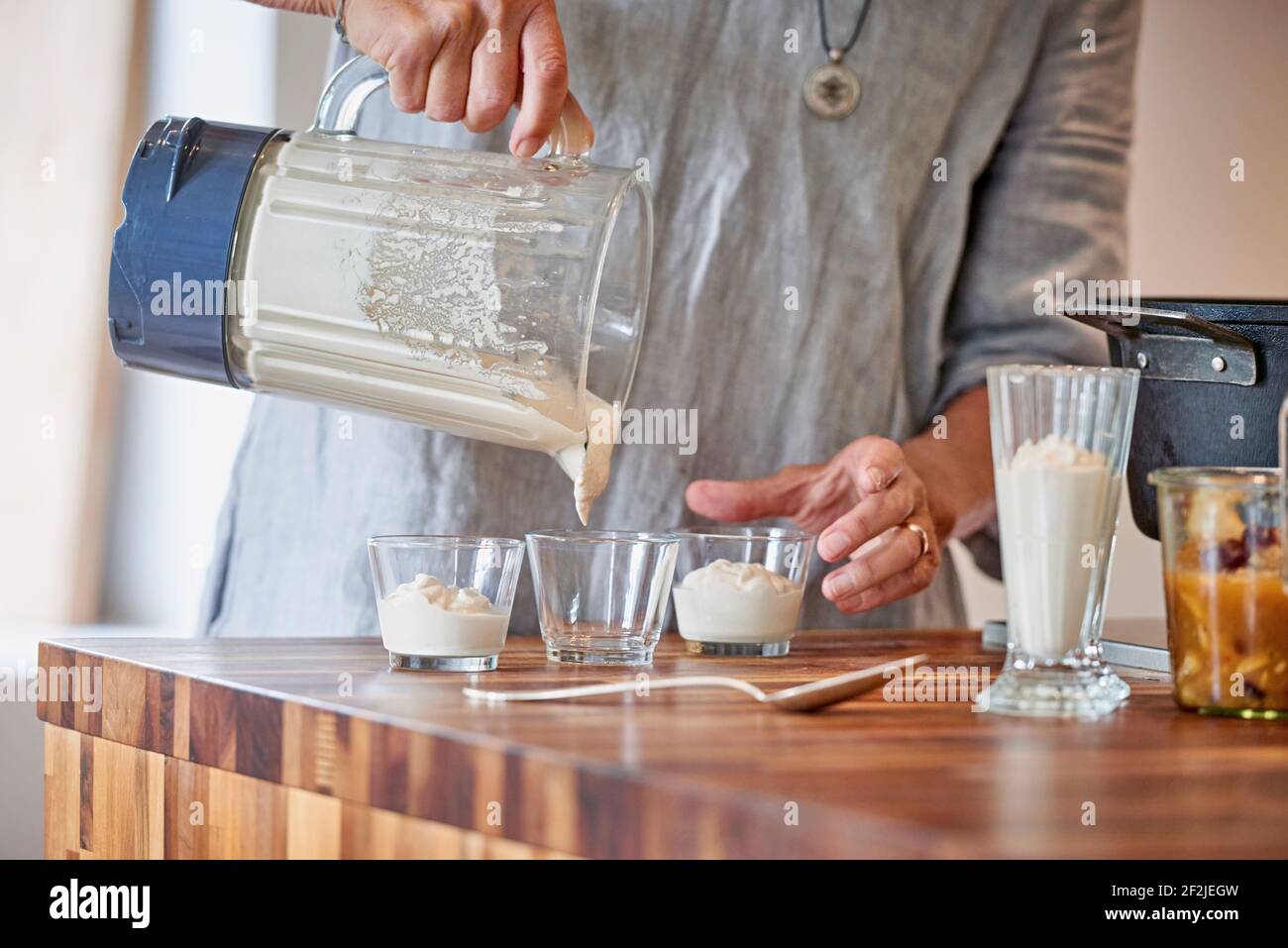 Die Hände der Frau füllen kleine Gläser mit Dessertcreme aus Mixbecher aus Glas Stockfoto