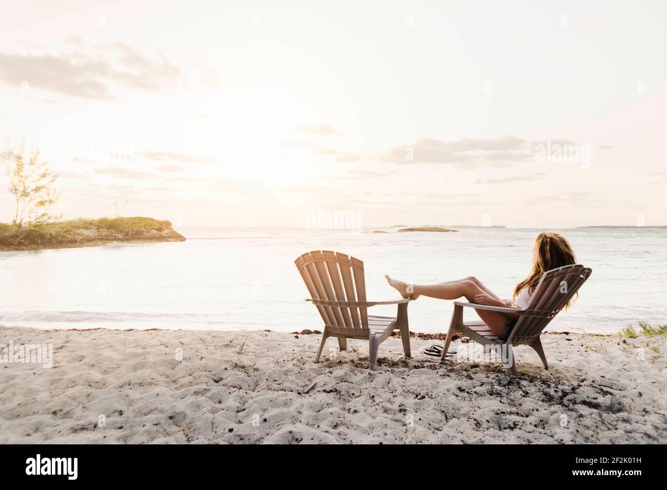 Junge Frau, die am Strand bei Sonnenuntergang auf Bahamas sitzt Stockfoto
