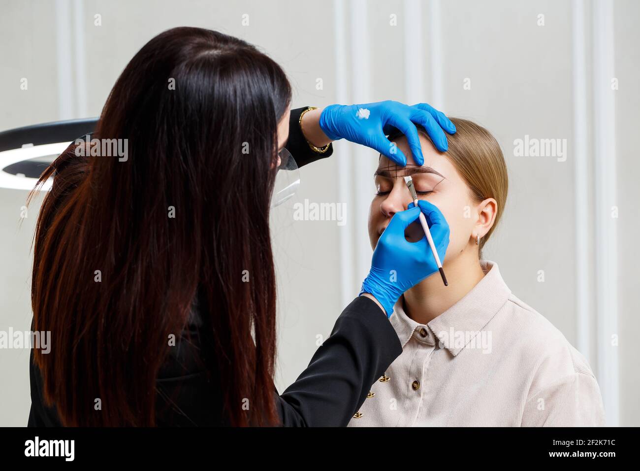 Eine Frau Permanent Make-up Künstlerin zeichnet eine Skizze der Augenbrauen auf das Gesicht ihres Kunden. Stockfoto