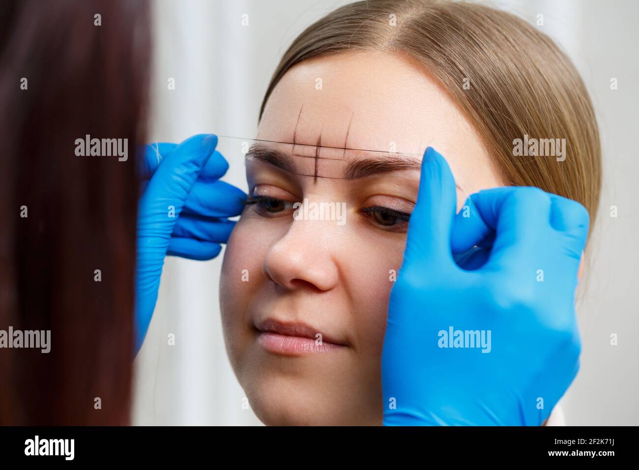Eine Frau Permanent Make-up Künstlerin zeichnet eine Skizze der Augenbrauen auf das Gesicht ihres Kunden. Stockfoto
