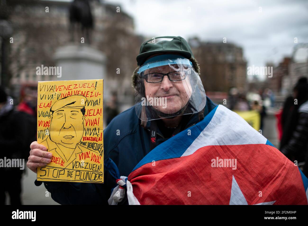Protestant in Gesichtsschild mit Plakat und mit kubanischer Flagge drapiert, bei Demonstration gegen US-Beteiligung in Kuba, Trafalgar Square, London, 12. Dezember Stockfoto