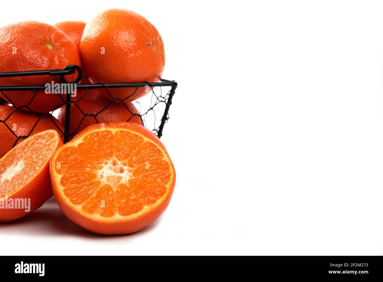 Ganze und in Scheiben geschnittene saftige frische Orangenfrüchte in einem schwarzen Metallkorb Stockfoto