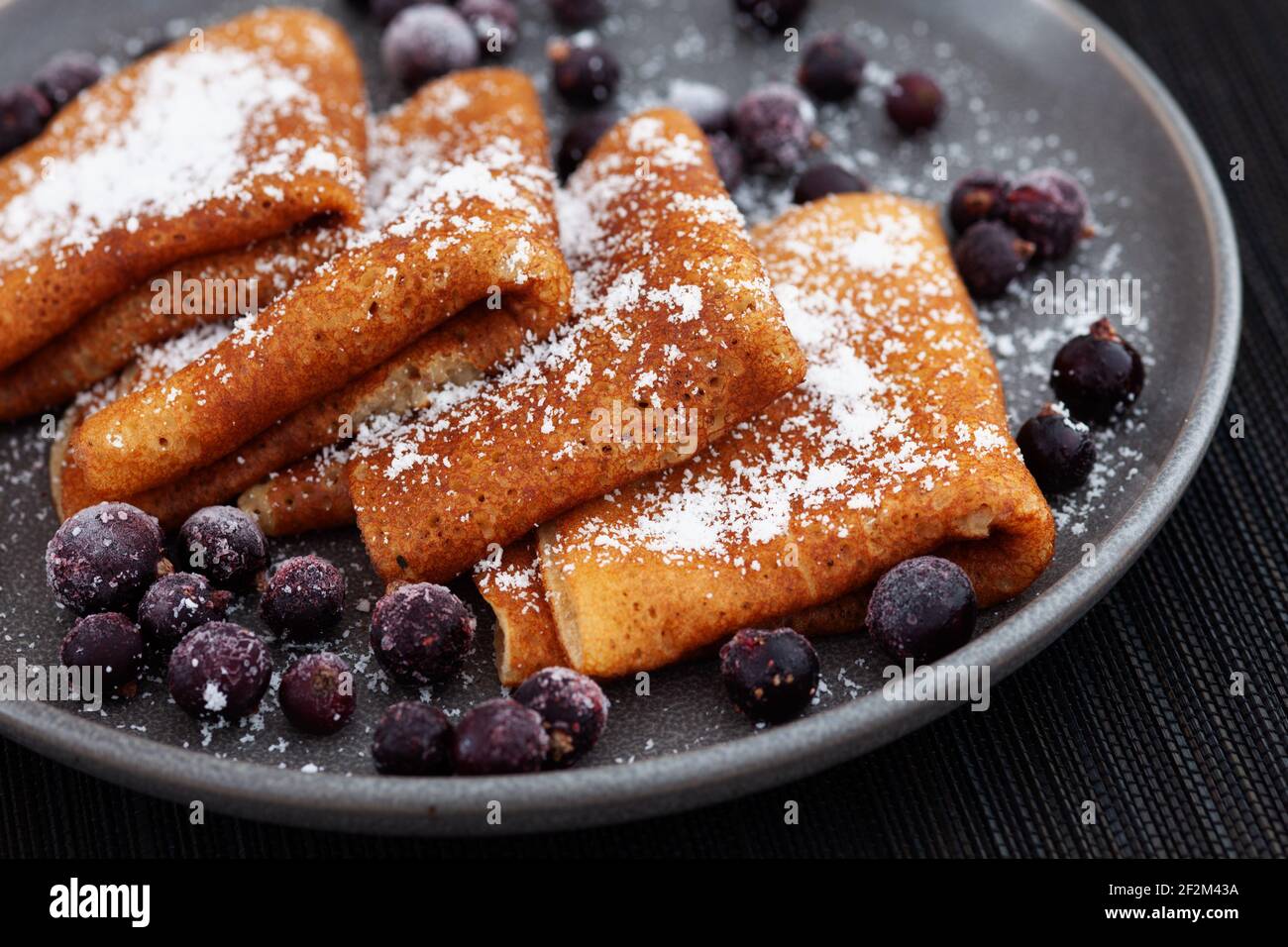 Pfannkuchen auf einem Teller mit Kokosflocken darauf und mit gefrorenen schwarzen Johannisbeeren um sie herum. Low-Taste. Nahaufnahme. Stockfoto