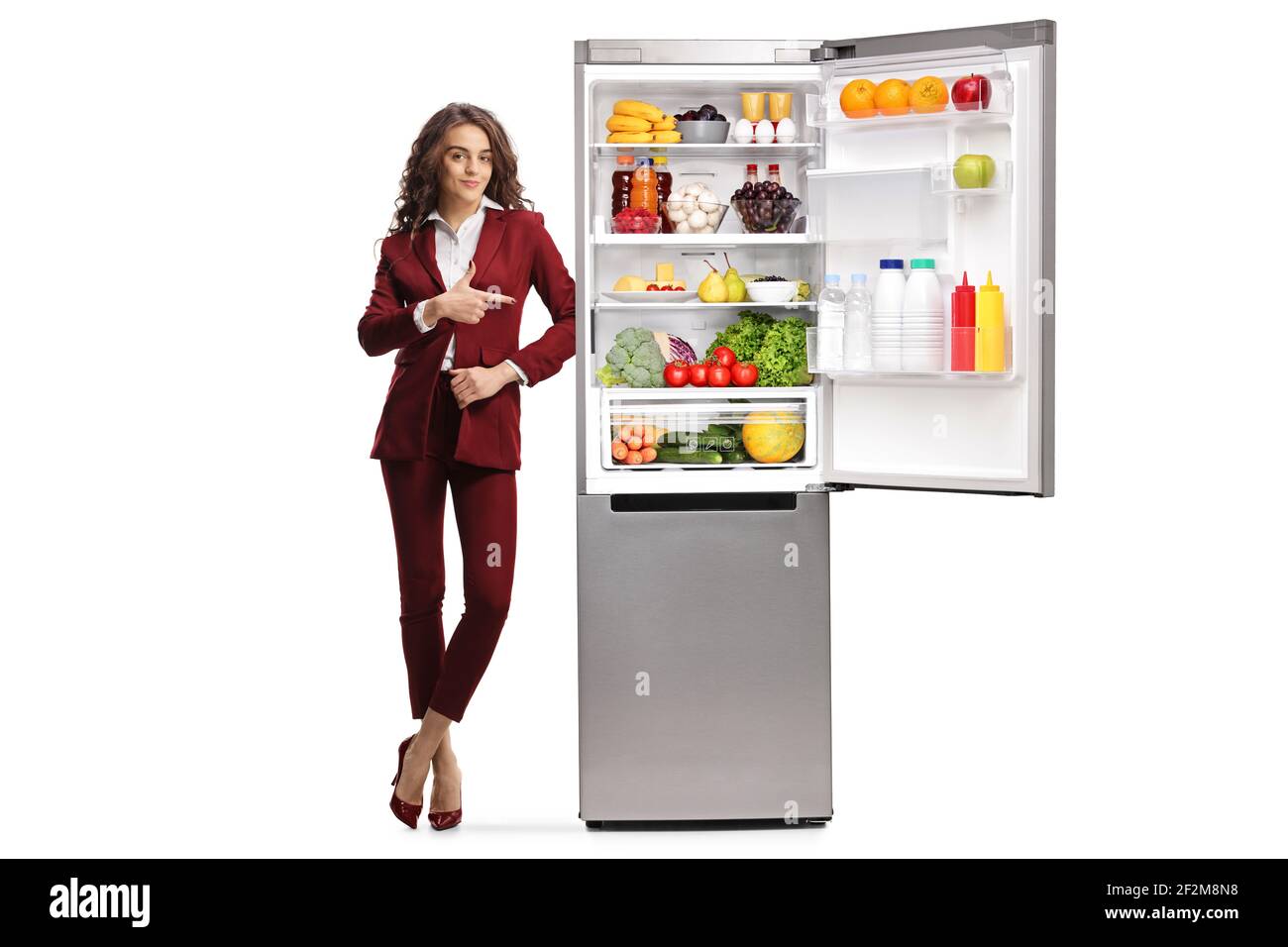 In voller Länge Porträt einer jungen Frau zeigt auf ein Kühlschrank mit Lebensmitteln isoliert auf weißem Hintergrund Stockfoto