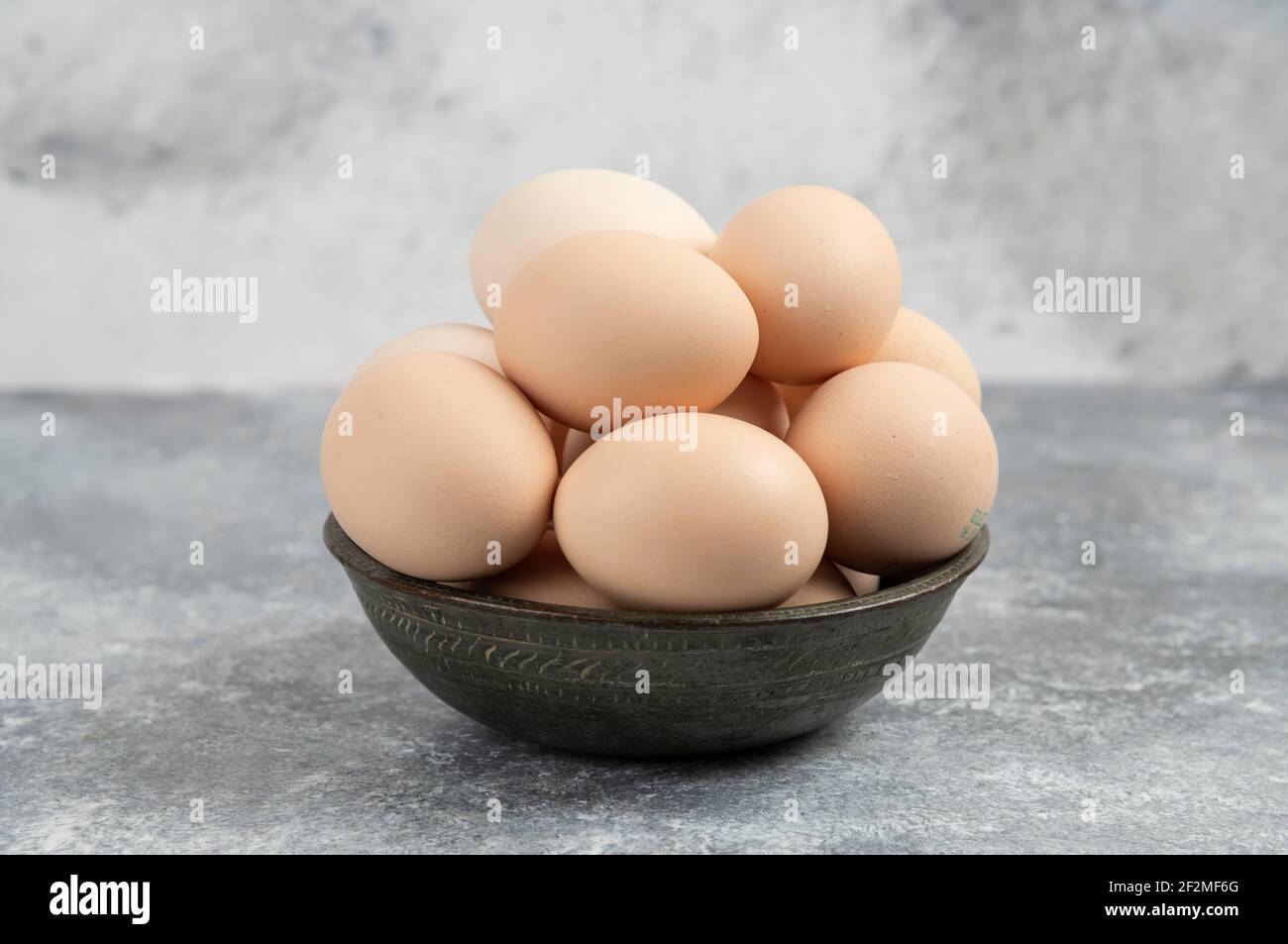 Dunkle Schüssel mit frischen ungekochten Eiern auf Marmorboden Stockfoto
