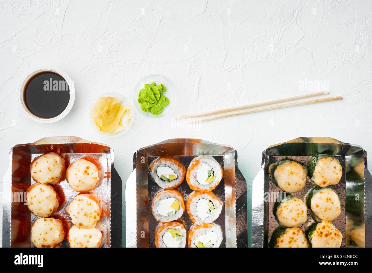 Sushi-Brötchen zum Mitnehmen in Behältern, philadelphia-Brötchen und gebackene Garnelenrollen Set, auf weißem Steingrund, Draufsicht flach liegend, mit Copyspace und s Stockfoto