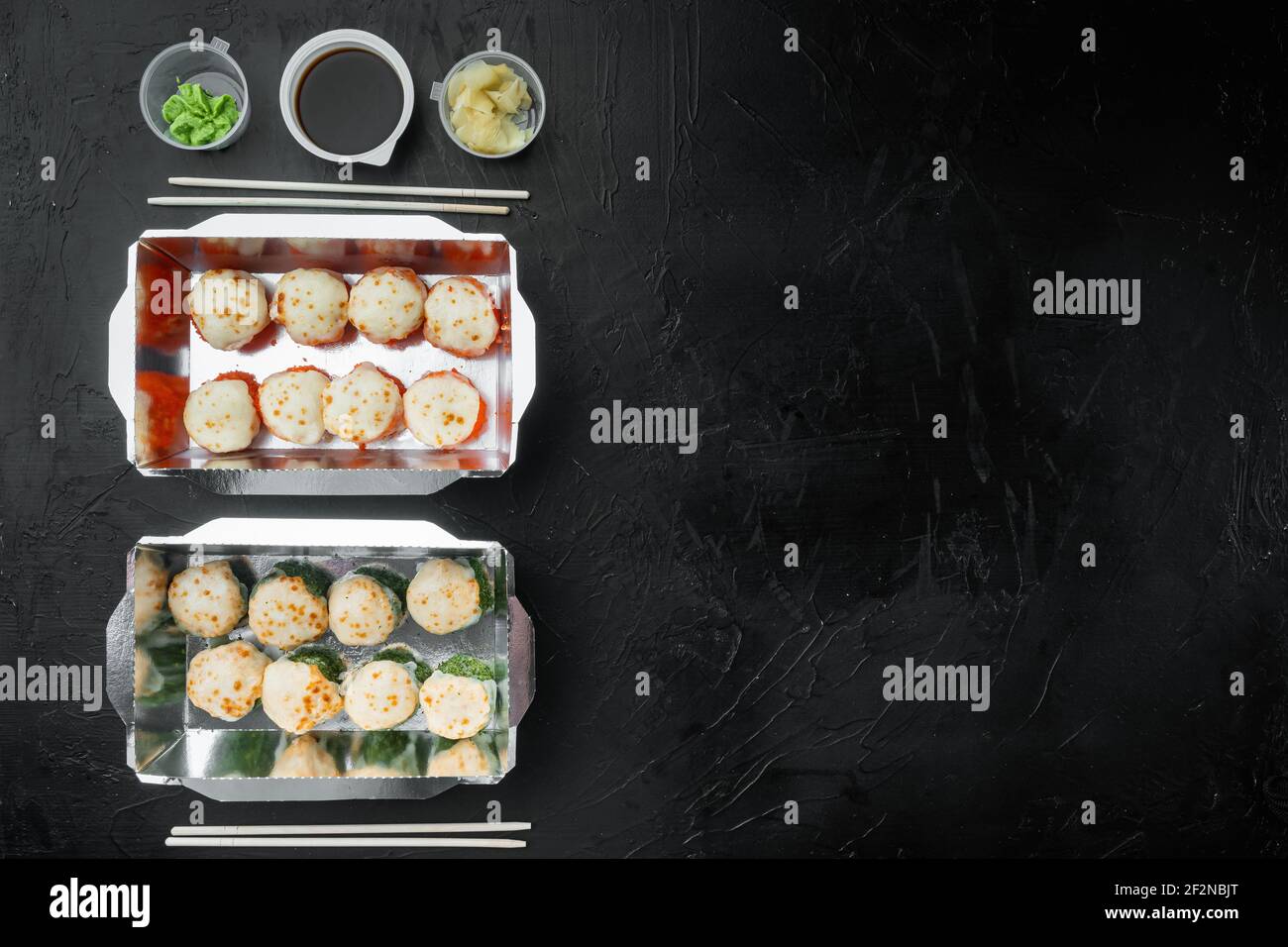 Leckere Sushi-Rollen in Einwegboxen Set, auf schwarzem Stein Hintergrund, Draufsicht flach legen, mit Copyspace und Platz für Text Stockfoto