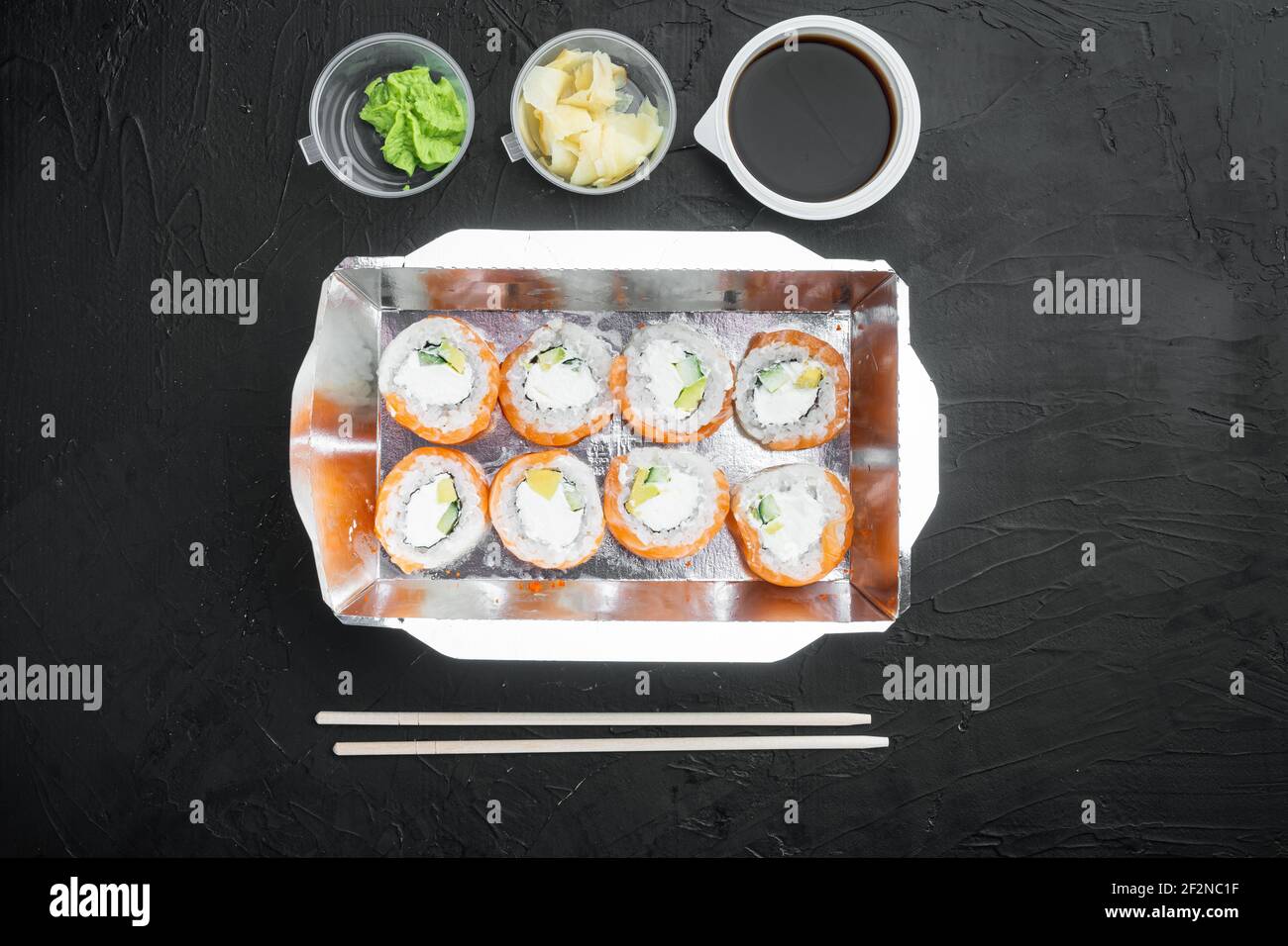 Sushi-Brötchen zum Mitnehmen in Behältern, philadelphia-Brötchen und gebackene Garnelenrollen Set, auf schwarzem Steinhintergrund, Draufsicht flach liegend, mit Copyspace und s Stockfoto