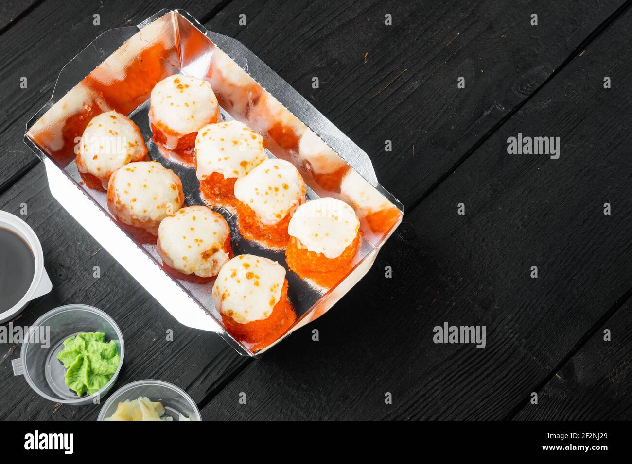 Leckere Sushi-Rollen in Einwegboxen Set, auf schwarzem Holztisch Hintergrund, mit Copyspace und Platz für Text Stockfoto