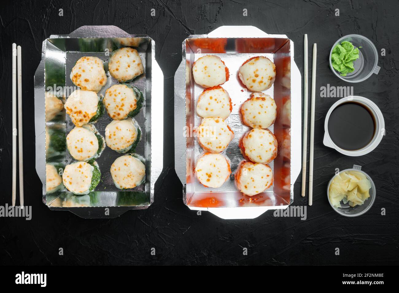 Sushi-Brötchen zum Mitnehmen in Behältern, philadelphia-Brötchen und gebackene Garnelenrollen, auf schwarzem Stein-Hintergrund, Draufsicht flach liegend Stockfoto