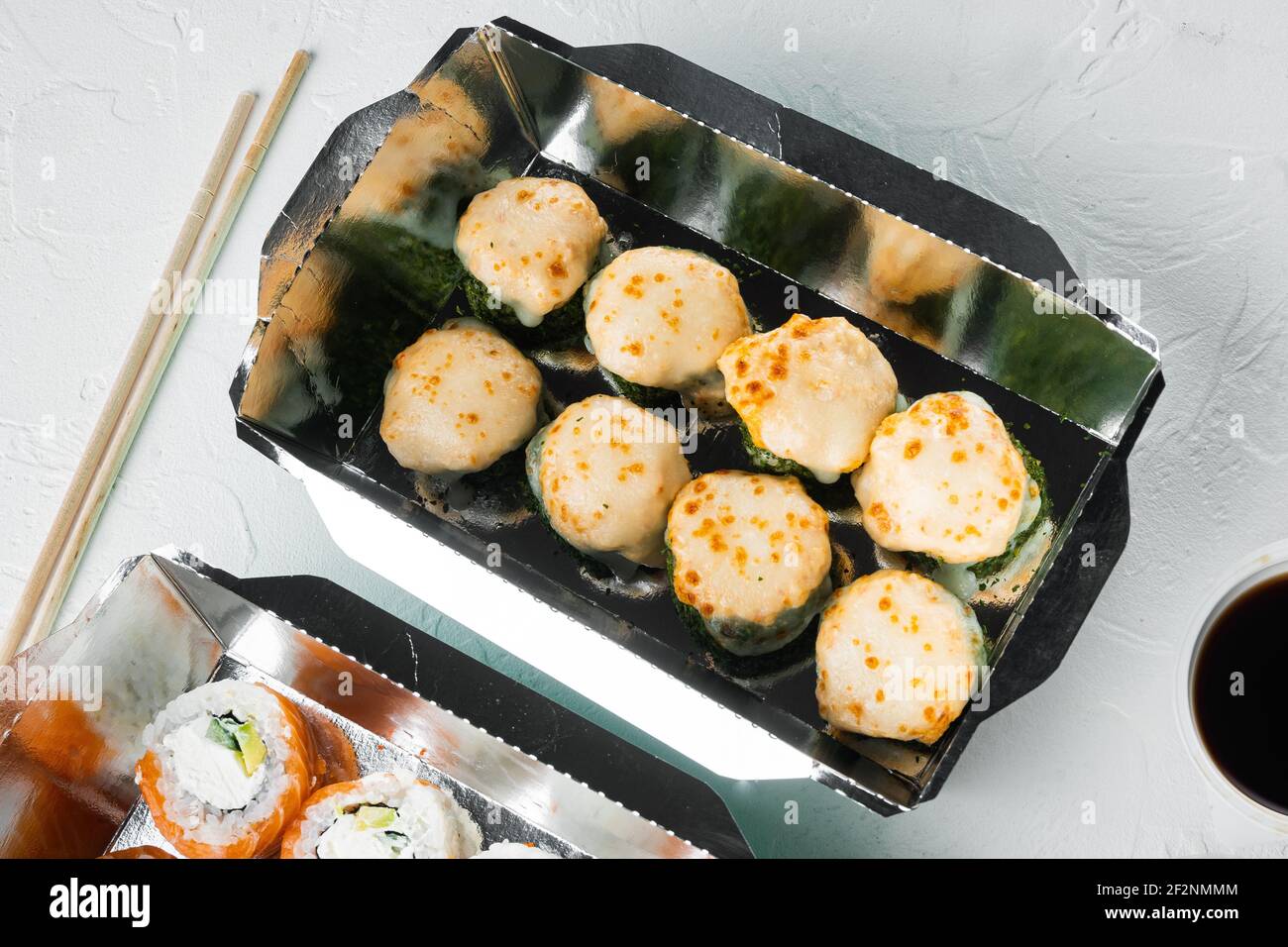 Vielfalt an verschiedenen Sushi und Brötchen, Lachs und Thunfisch in Lieferung Food-Konzept-Set, auf weißem Stein Hintergrund Stockfoto