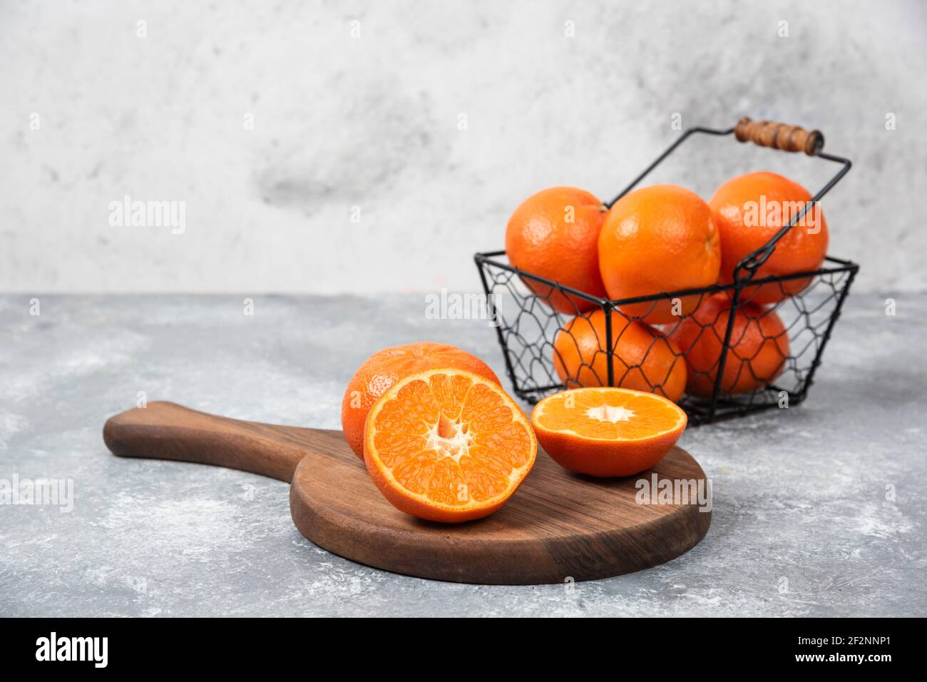 Ein metallischer schwarzer Korb voller saftiger oranger Früchte Steinhintergrund Stockfoto