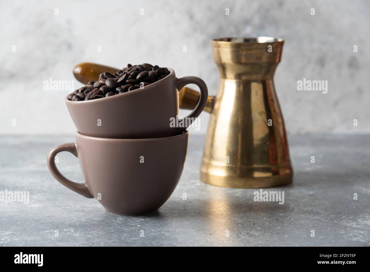 Tasse voll mit Kaffeebohnen und Kaffeemaschine auf Marmor Hintergrund Stockfoto