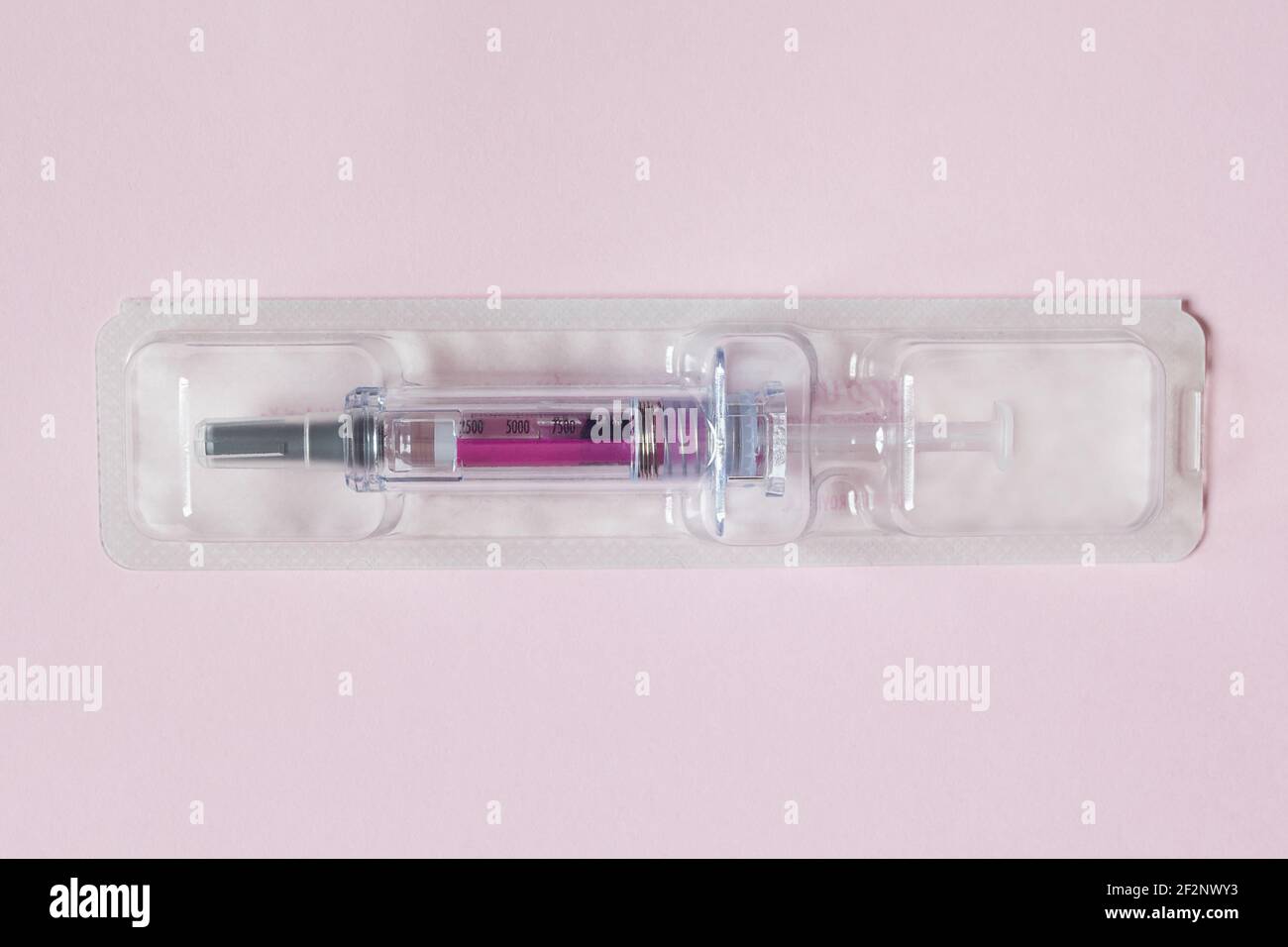 Einzeln versiegelte Spritze mit einer medizinischen Lösung in einem Kunststoff-Blister auf einem strukturierten rosa Papier Hintergrund vorgefüllt. Wissenschaft Gesundheit und Medizin. Stockfoto