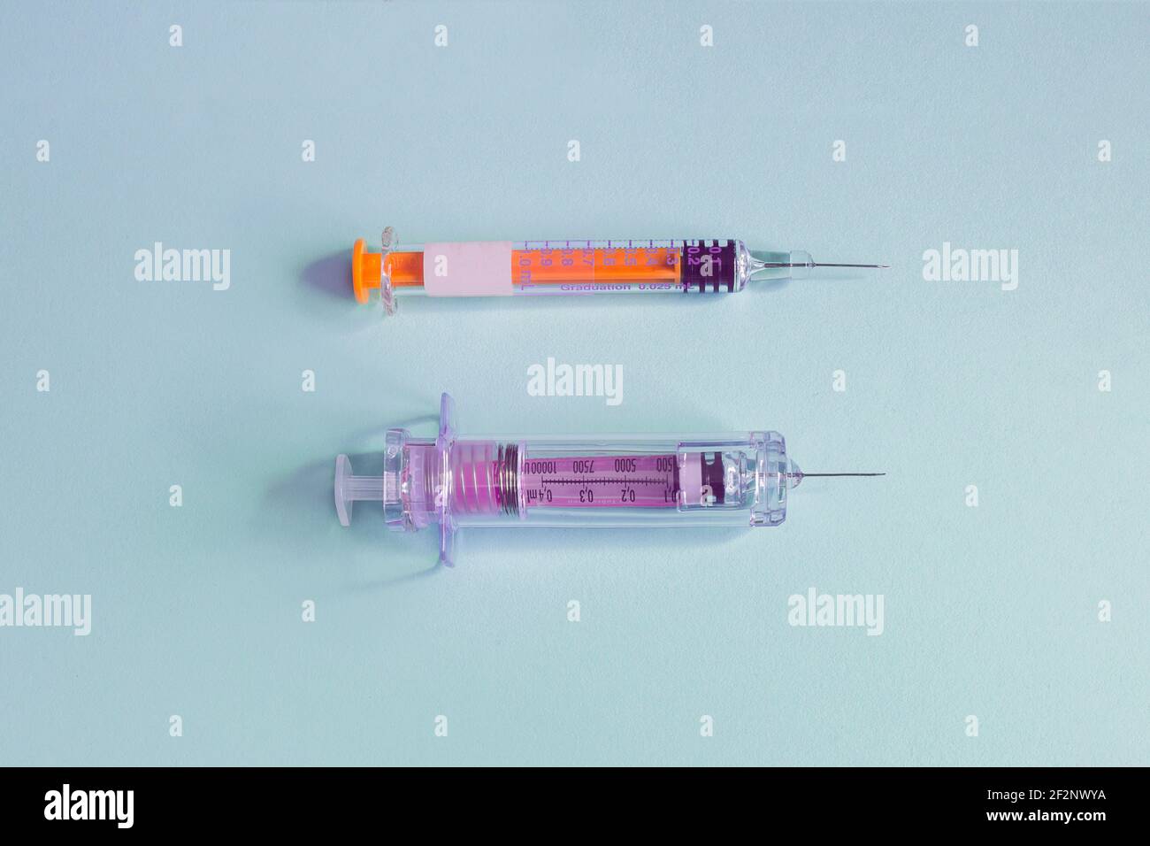 Zwei verschiedene Impfspritzen mit der Nadel auf einem texturierten blauen Papierhintergrund. Gesundheitswissenschaften und Medizin. Stockfoto