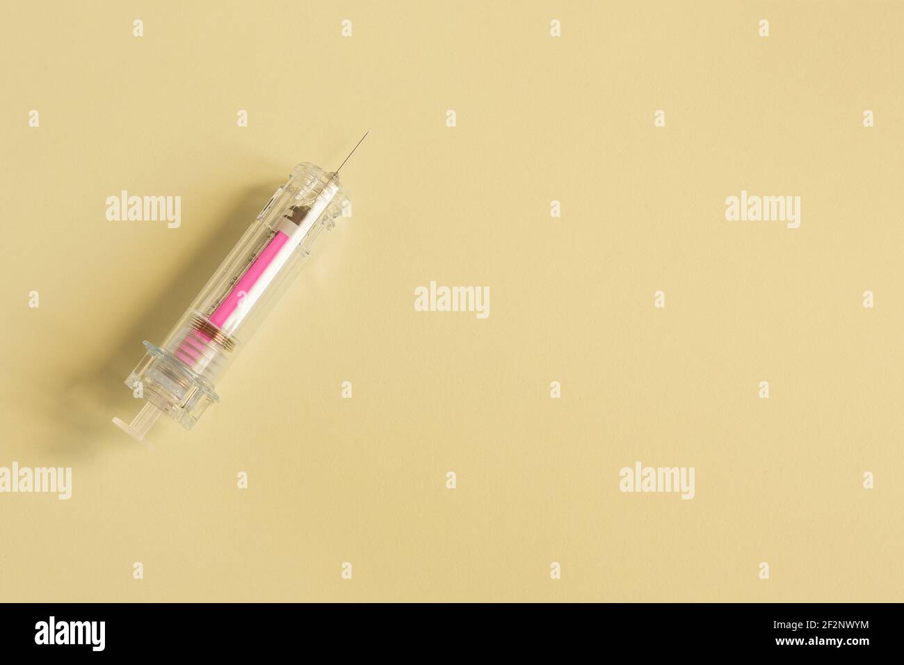 Eine bunte isolierte rosa Spritze mit der Nadel auf texturiertem gelbem Papierhintergrund und Platz, um einen Text einzufügen. Gesundheitswissenschaften. Stockfoto
