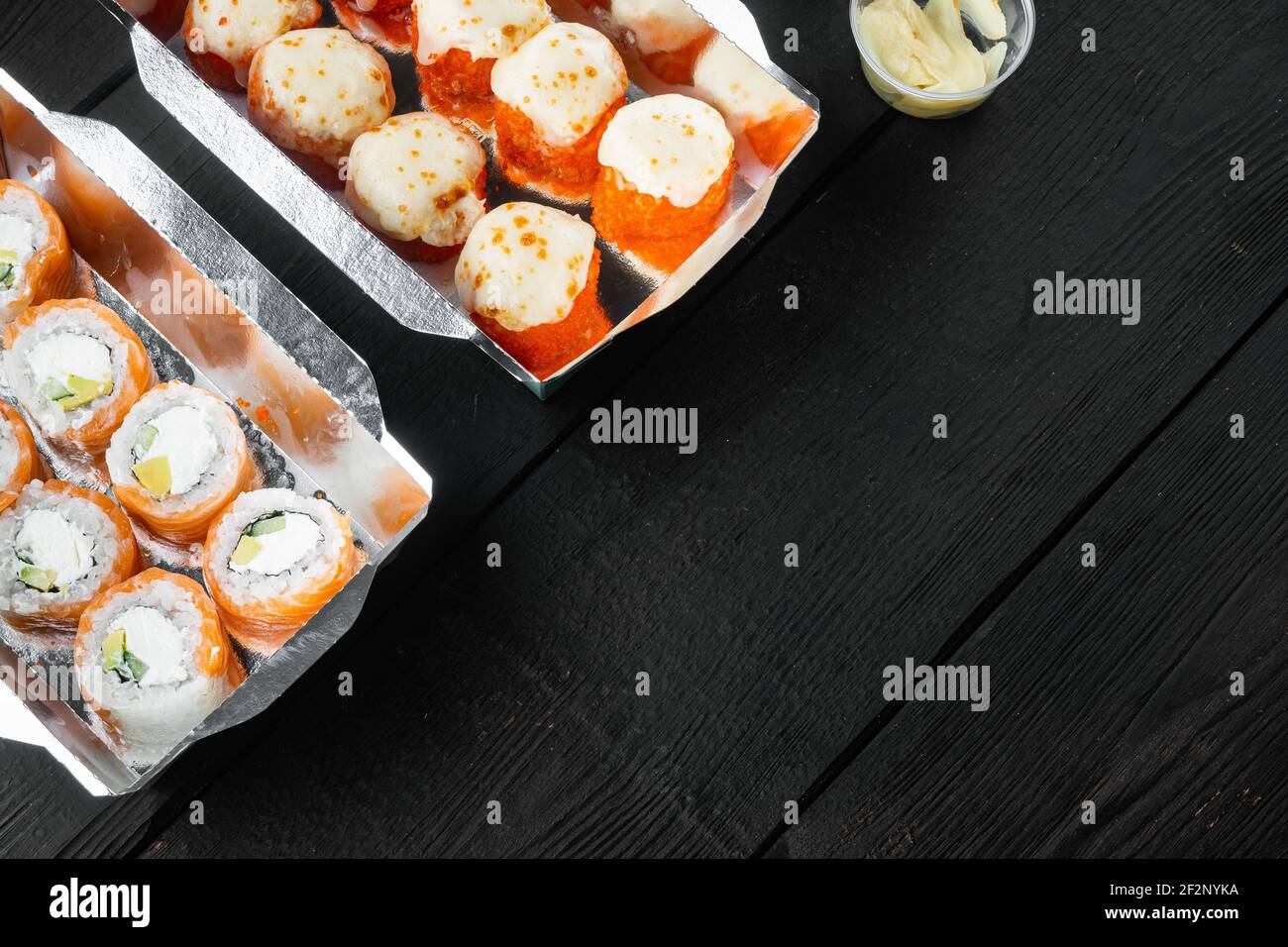 Leckere Sushi-Rollen in Einwegboxen Set, auf schwarzem Holztisch Hintergrund, mit Copyspace und Platz für Text Stockfoto
