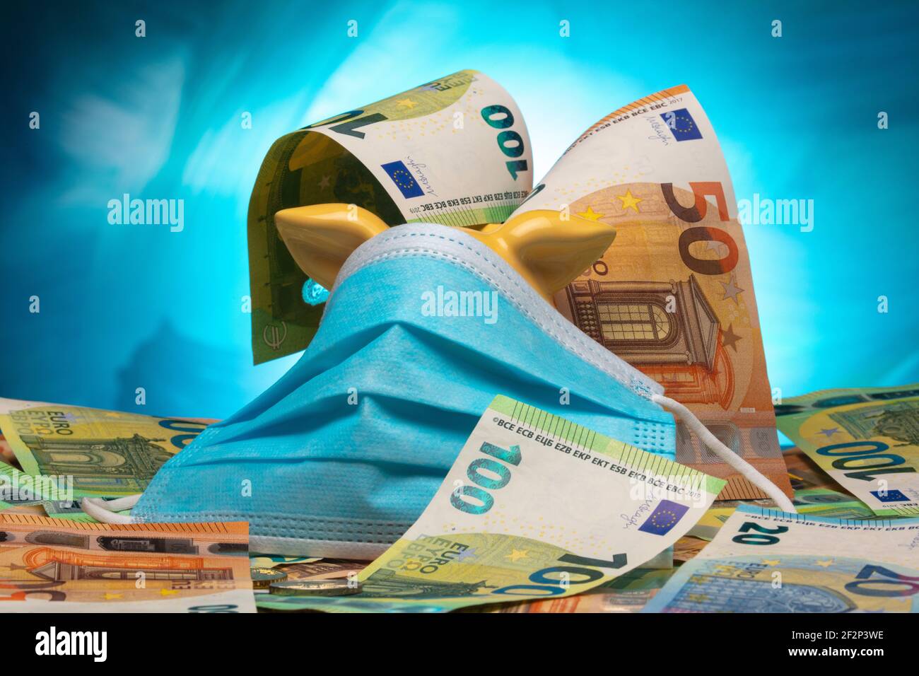 Sparschwein mit blauem Mund- und Nasenschutz und Euro-Banknoten vor blauem Hintergrund. Stockfoto