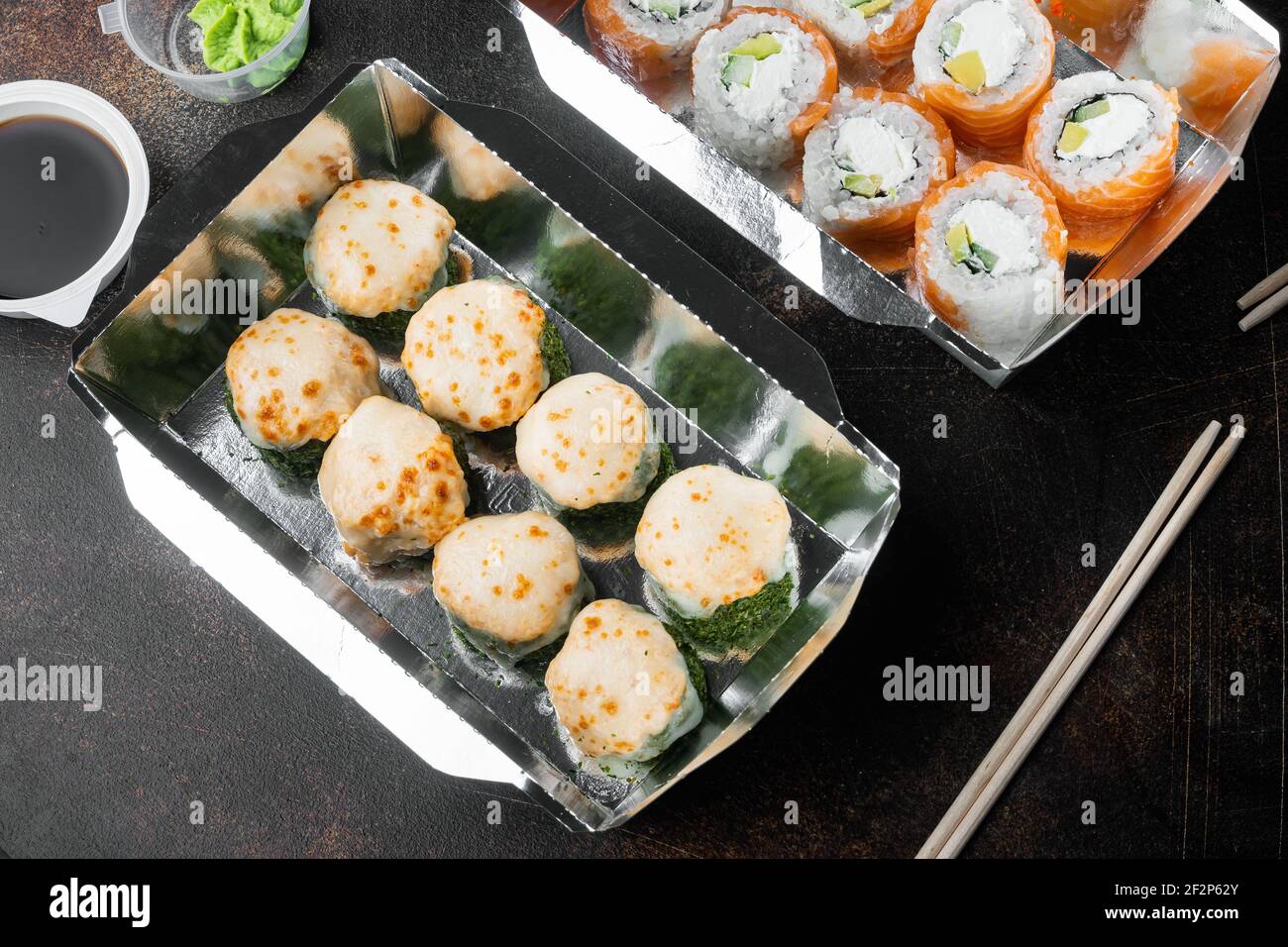 Sushi-Brötchen zum Mitnehmen in Behältern, philadelphia-Brötchen und gebackene Garnelenrollen auf altem dunklen rustikalen Hintergrund Stockfoto