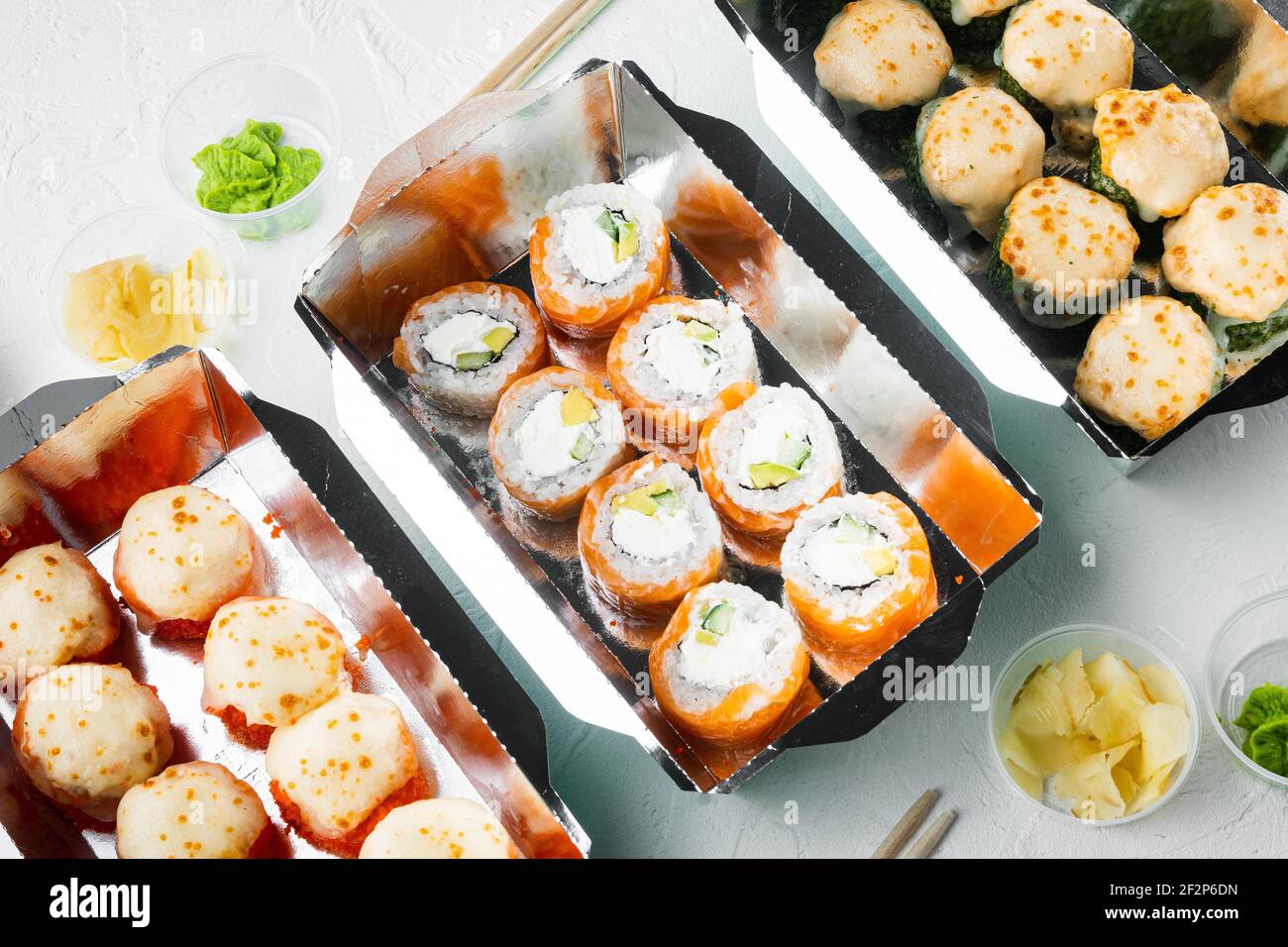 Leckere Sushi-Rollen in Einwegboxen Set, auf weißem Stein Hintergrund Stockfoto