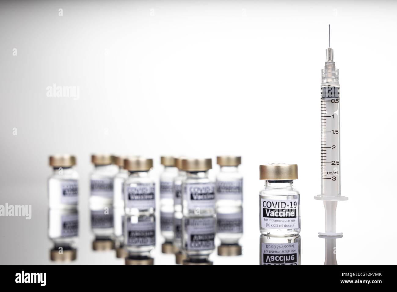 Konzentrieren Sie sich auf ein Covid-19-Impfstofffläschchen mit Spritze, mit mehreren verschwommenen Fläschchen im Hintergrund Stockfoto