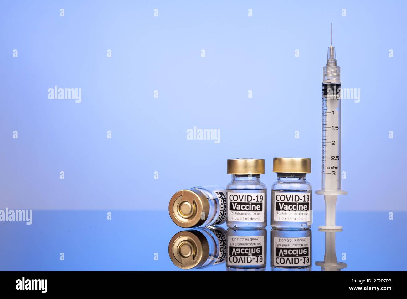 Covid-19 Impfstofffläschchen mit Spritzenkonzept auf reflektierender Oberfläche Blauer Hintergrund Stockfoto