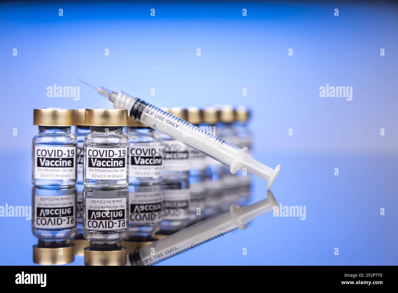 Covid-19 Impfstofffläschchen mit Spritzenkonzept auf blauer reflektierender Oberfläche. Konzentrieren Sie sich auf die erste Reihe mit geringer Schärfentiefe Stockfoto