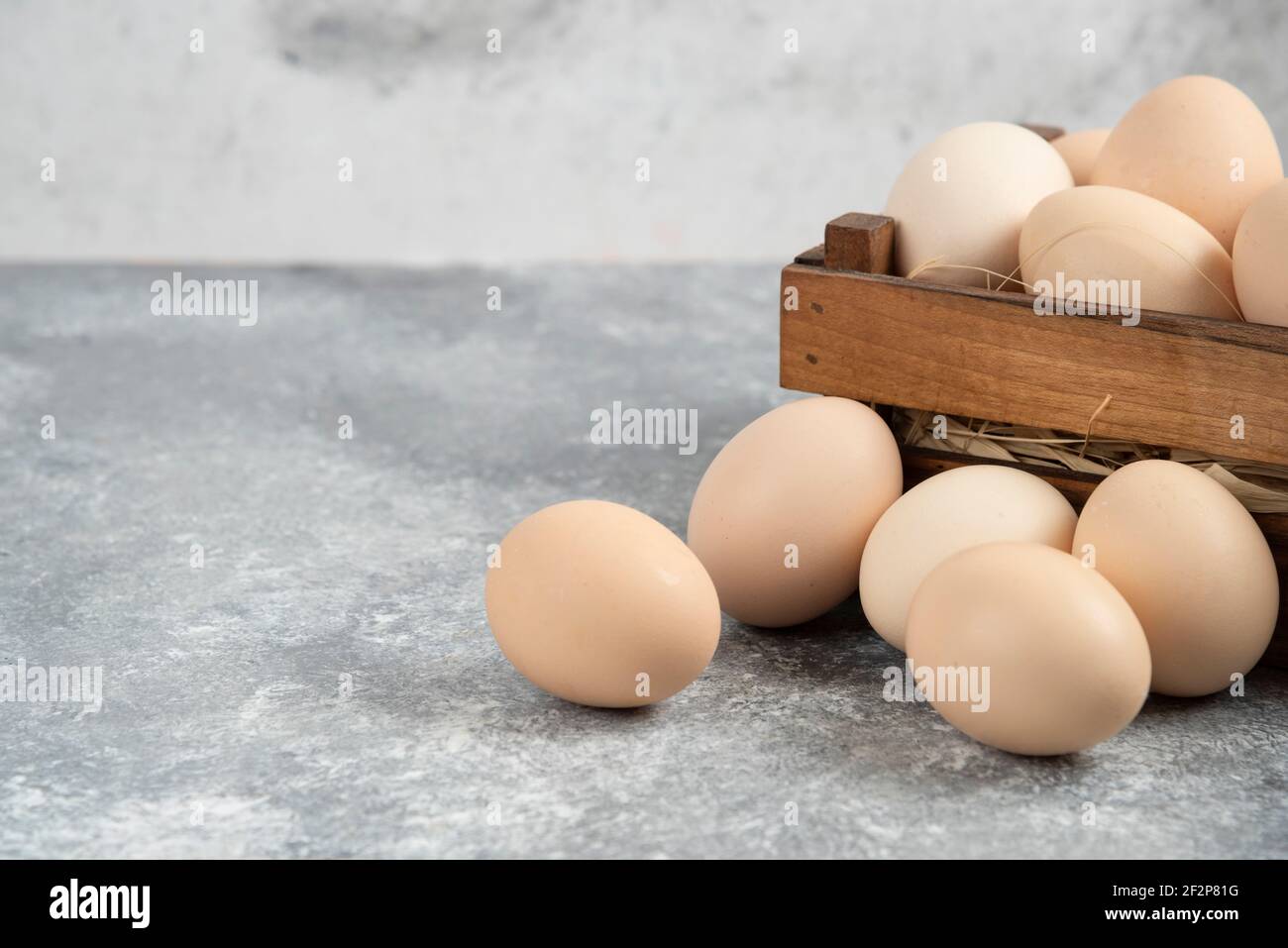 Holzkiste mit Bio-rohen Eiern auf Marmoroberfläche Stockfoto