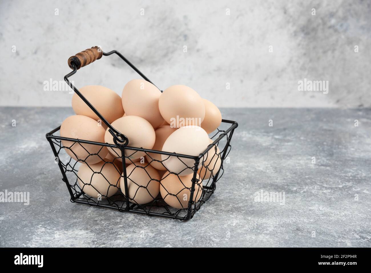 Metallkorb mit frischen Bio-rohen Eiern auf Marmoroberfläche Stockfoto