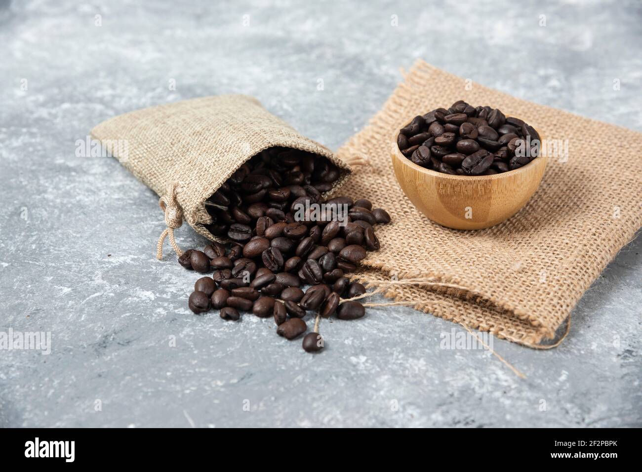 Geröstete Kaffeebohnen aus Sackleinen und in einer Schüssel Auf Marmorboden Stockfoto