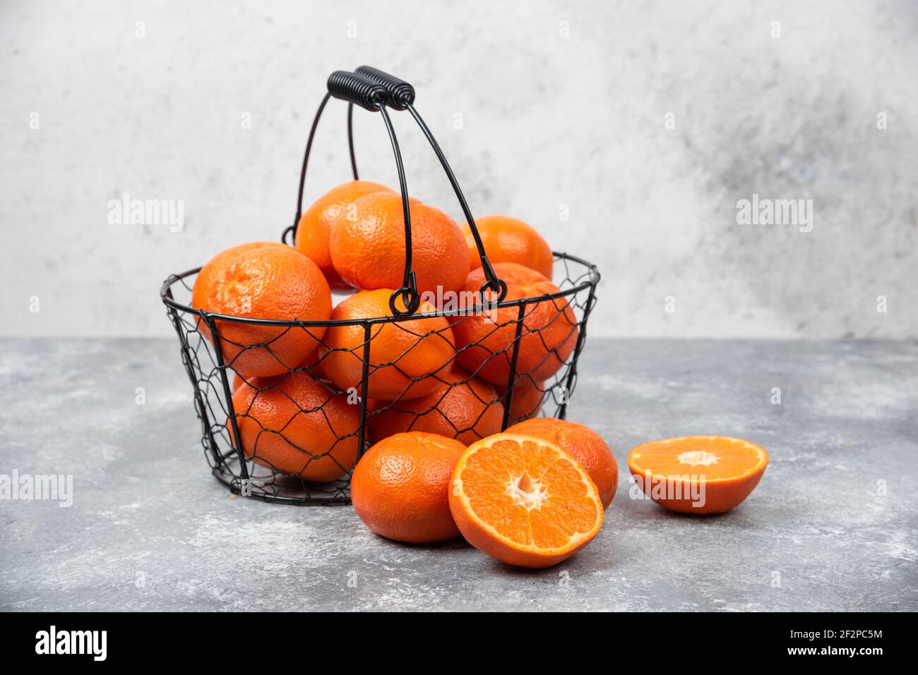 Ein metallischer schwarzer Korb voller saftiger oranger Früchte Steinhintergrund Stockfoto