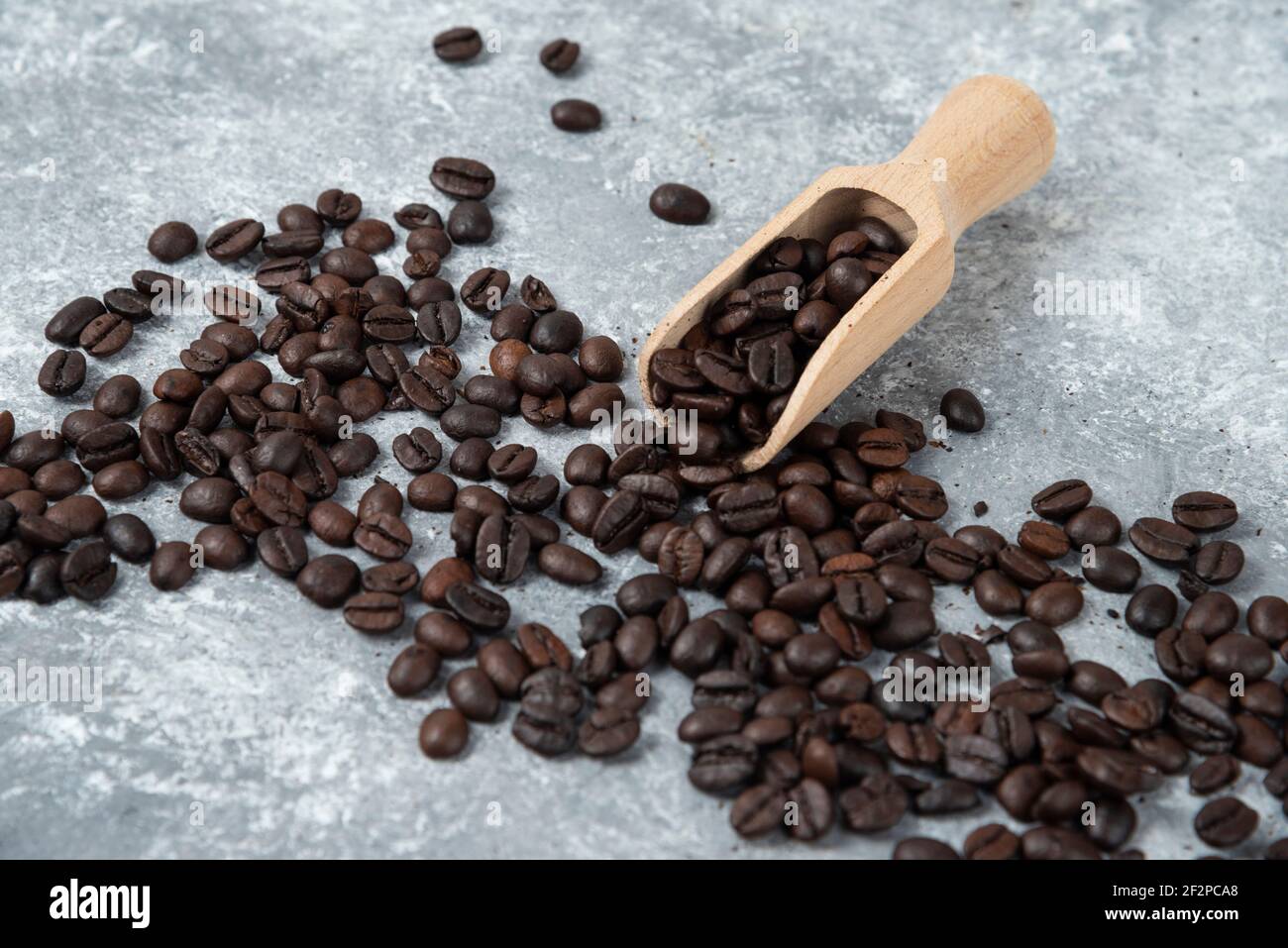 Holzlöffel und verstreute geröstete Kaffeebohnen auf Marmoroberfläche Stockfoto