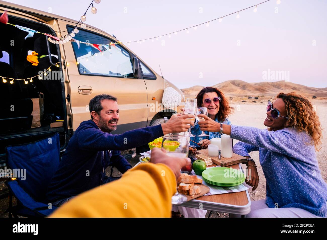 Gruppe von erwachsenen kaukasischen Menschen Freunde genießen und feiern zusammen In Freundschaft im Freien mit Tisch und Essen und Van Fahrzeug Around - fröhlich und Toasting während des Urlaubs Mittagessen Stockfoto