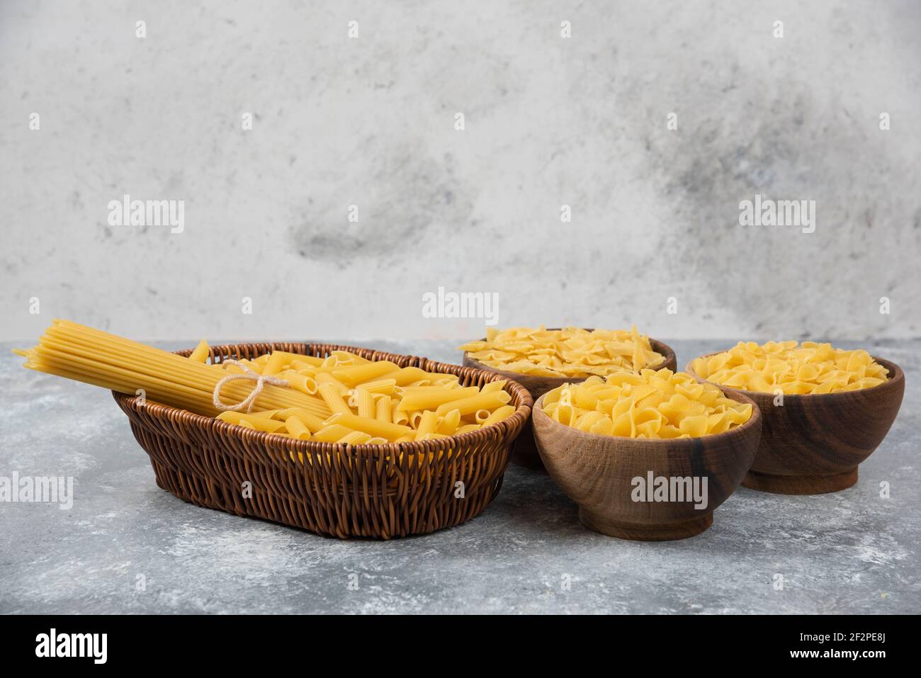 Stapel von verschiedenen ungekochten trockenen Nudeln in Korbkorb und Holzschüsseln Stockfoto