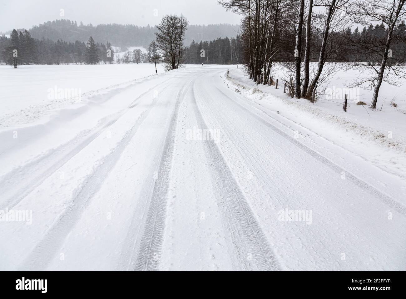 Deutschland, Bayern, schneebedeckte Landstraße mit Reifenpfaden. Stockfoto