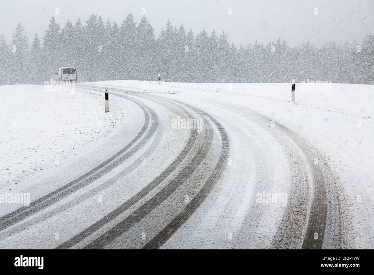 Deutschland, Bayern, Auto auf schneebedeckter Landstraße mit Reifenspuren. Stockfoto