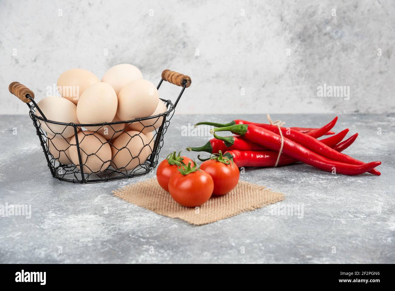 Korb mit frischen ungekochten Eiern, Chilischoten und Tomaten auf Marmorboden Stockfoto