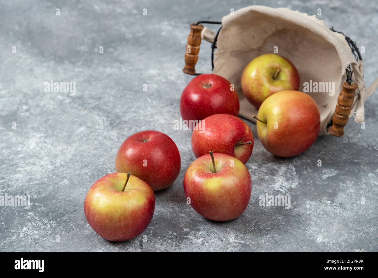Haufen frischer reifer Äpfel aus dem Korbkorb auf Marmoroberfläche Stockfoto