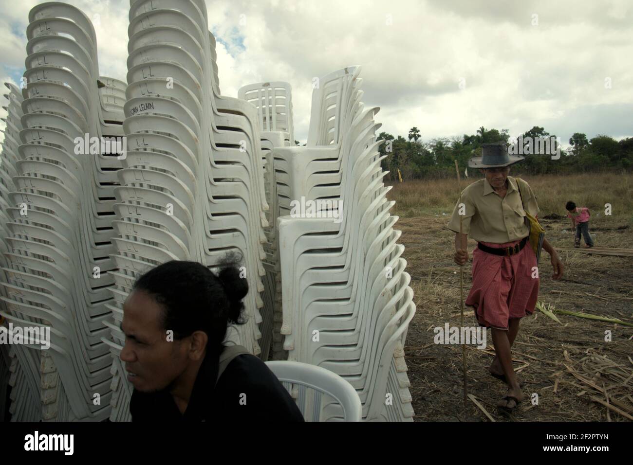 Ein Arbeiter und ein Dorfbewohner, die gerade dabei sind, eine zeremonielle Veranstaltung zu sehen, an der indonesische Beamte teilnehmen werden, um sich um Stapel von Plastikstühlen vorzubereiten. Stockfoto