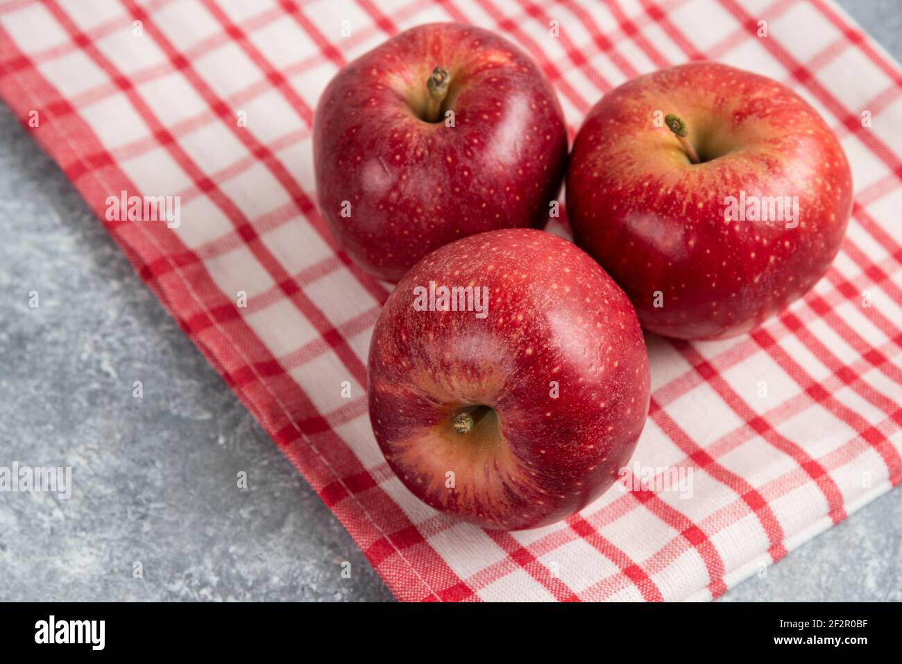 Drei rote Äpfel mit gestreifter Tischdecke auf Marmoroberfläche Stockfoto