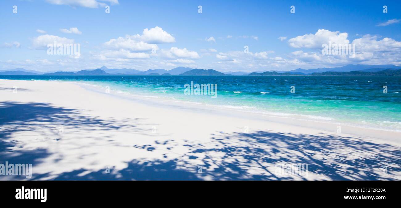 Ein ruhiges tropisches Meer im sonnigen Sommer. Leerer weißer Sandstrand und weiße Wolken am blauen Himmel im Hintergrund. Abstrakter Schatten am Strand. Stockfoto