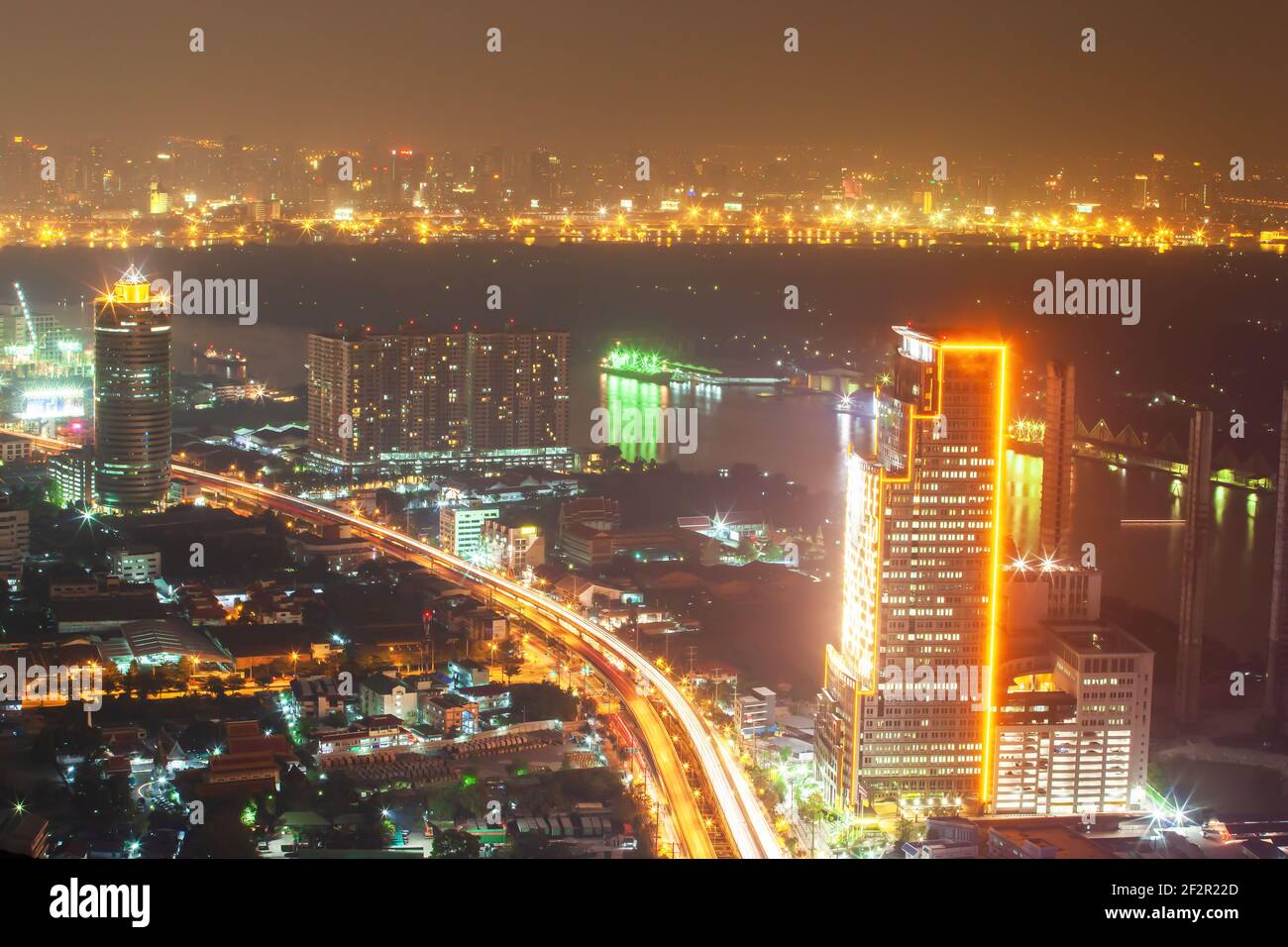 Stadtnacht am Flussufer. Luftaufnahme der Innenstadt von Bangkok Gebäude und Chao Phraya Fluss in der Nacht. Leuchtende Neonlichter und Lichter Wanderwege auf der Straße. Stockfoto